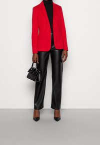Czerwona dopasowana marynarka, czarny golf, czarne spodnie z ekoskóry, czarne szpilki i mała czarna torebka. Gładkie tekstury na całej powierzchni.