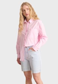Light pink long-sleeve button-up shirt with a pocket, paired with light blue denim shorts. Smooth texture, collared design, and relaxed fit.