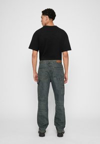 Black cotton t-shirt and dark blue cargo jeans with patch pockets, belt loops, and slight wash detailing, viewed from behind.