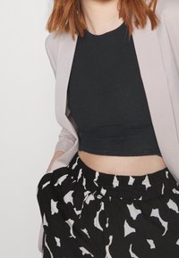 Zwarte geribbelde crop top onder een lichtroze blazer, gecombineerd met zwarte broeken met een wit abstract patroon en een elastische tailleband.