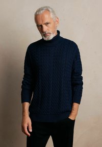 Granatowy sweter z golfem, wykonany w splot kablowym, z prążkowanymi mankietami i dołem, charakteryzujący się teksturowanymi wzorami oraz luźnym krojem.