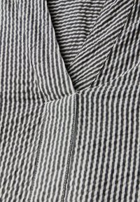 Tessuto a righe bianche e nere con una texture stropicciata, caratterizzato da linee verticali e un design a V, che mette in risalto i dettagli delle cuciture.