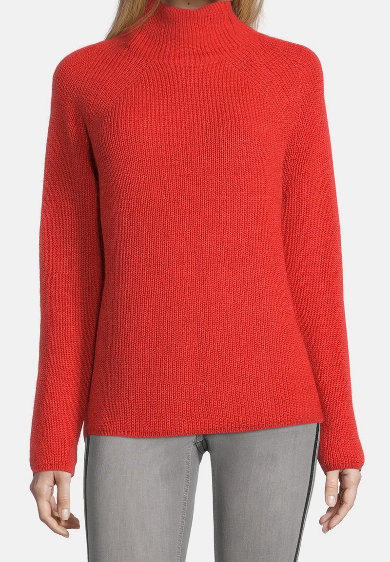 Maglione rosso lavorato a maglia con collo alto, texture a coste, maniche lunghe e vestibilità comoda, abbinato a jeans grigi.