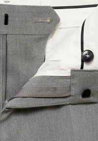 I pantaloni grigi presentano una chiusura con cerniera, dettaglio con bottone e una fodera in tessuto bianco. Una piping nera a contrasto è visibile lungo i bordi.