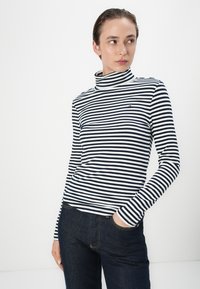 Bluză cu guler înalt, cu dungi alb-negru, textură canalată, cu un mic accent de logo; asortată cu blugi din denim închis.