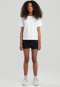 White cotton t-shirt with "SUMMER ESCAPE" text, paired with black denim shorts, white sneakers, and blue-striped socks.