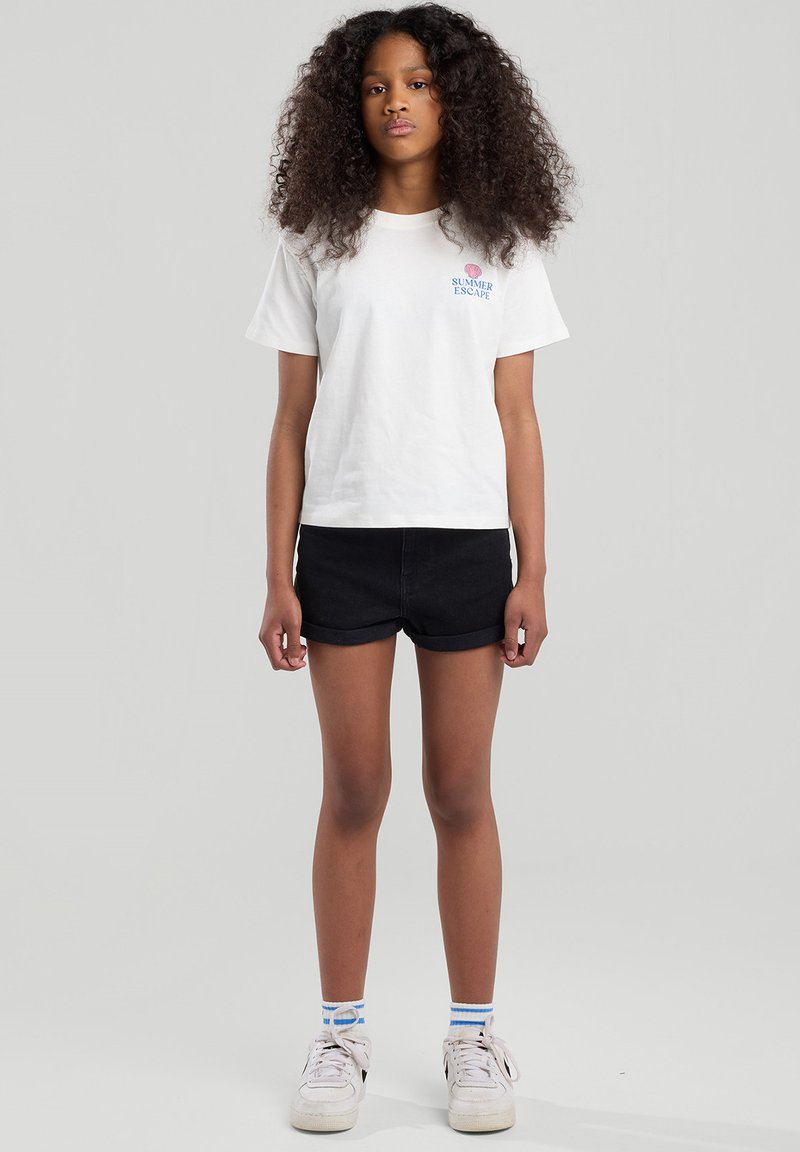 White cotton t-shirt with "SUMMER ESCAPE" text, paired with black denim shorts, white sneakers, and blue-striped socks.