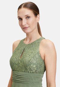 Robe en dentelle verte avec un détail en trou de serrure au niveau du col, présentant un corsage ajusté et une jupe fluide, mettant en valeur des motifs floraux complexes.