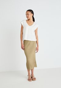 Top bianco a maniche corte con scollatura a V e bordo in pizzo abbinato a una gonna beige a coste lunga fino alla caviglia e sandali con cinturino.