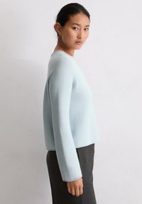 Jasnoniebieski sweter o fakturowanym splocie z okrągłym dekoltem i długimi rękawami, w połączeniu z dopasowaną ciemnoszaryą spódnicą ołówkową.