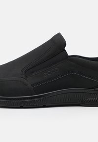 Chaussure noire en cuir à enfiler avec des panneaux latéraux texturés, des coutures contrastées et une semelle en caoutchouc avec une adhérence à motif.