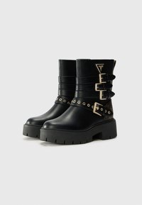 Bottes noires en cuir à la cheville avec trois boucles décoratives, bout rond, semelle épaisse, accents en métal doré et détails latéraux à motif.