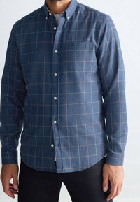 Camicia button-up in tessuto blu con motivo a rete in rosso e giallo. Presenta un colletto, maniche lunghe e una tasca sul petto.