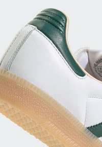 Sneaker in pelle bianca e verde con suola in gomma testurizzata. Presenta dettagli cuciti e un accento verde liscio sulla parte posteriore.