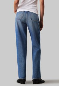 Jeans de mezclilla azul claro con un corte recto, que cuentan con dos bolsillos traseros y un ligero desvanecimiento. Combinados con botas negras de tobillo.