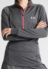 Pullover grigio a maniche lunghe con collo sollevato. Presenta una mezza zip con accenti rossi e logo. Realizzato in tessuto sportivo testurizzato.