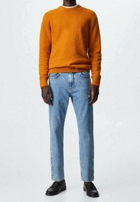 Pull en maille orange à col rond, associé à un jean en denim bleu clair et des chaussures en cuir noir, avec une coupe droite.