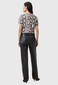 Korte mouw shirt met een beige en zwarte slangenprint, gecombineerd met hoog opgesneden zwarte leren broek met studs accenten.