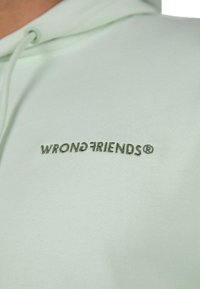 Felpa verde menta con texture morbida, con un logo ricamato centrato che recita "WRONGFRIENDS®" in un verde scuro a contrasto.