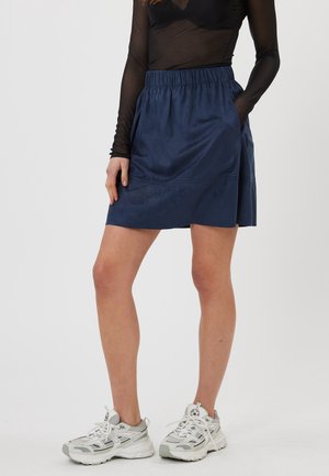 Jupe bleu marine avec une taille élastique, poches latérales et texture lisse, associée à des baskets grises et un haut à manches longues noir.