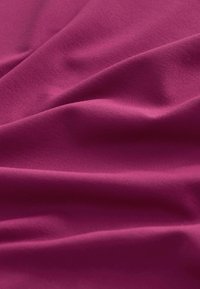 Tela lisa y profunda de color magenta con pliegues suaves y textura fina, mostrando reflejos de luz natural en la superficie.