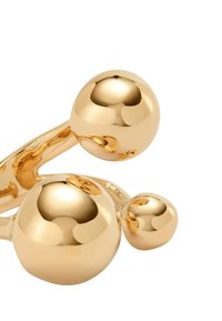 Escultura abstracta de metal dorado con tres esferas pulidas conectadas de diferentes tamaños sobre un fondo blanco.