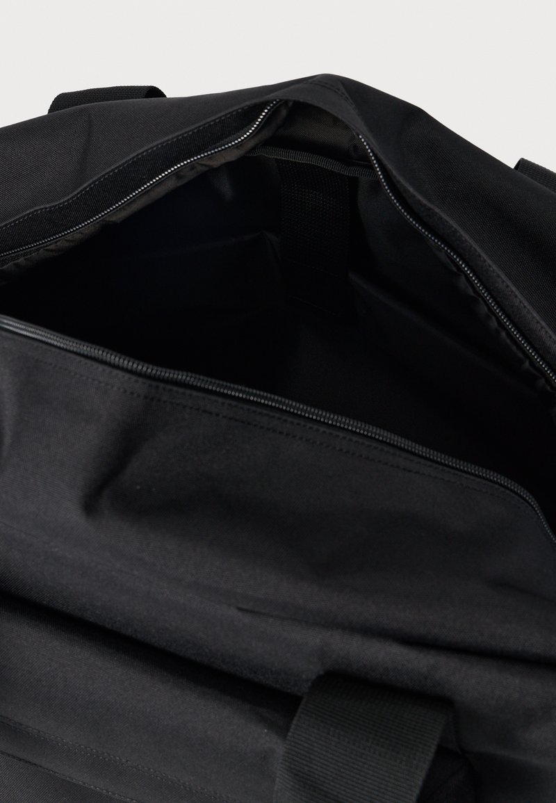 Zwarte rugzak met open rits, waarbij het ruime interieur en de stoffen riemdetail zichtbaar zijn tegen een neutrale achtergrond.