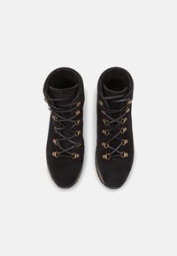 Bottes basses en daim noir avec lacets gris, œillets en métal et semelle texturée. Dotées d'un col matelassé pour le confort.