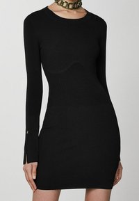Abito in maglia nera a coste con maniche lunghe, caratterizzato da spaccature laterali ai polsini e un design aderente che segue le forme del corpo.