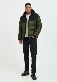Parka imbottita in verde oliva e nero, con cappuccio, tasche con zip e un design trapuntato. Abbinata a jeans neri e stivali neri.