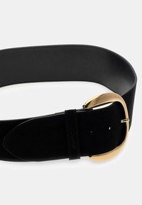 Zwarte suede riem met een glanzende gouden gesp, met een gladde textuur en een breed ontwerp. Inclusief merkvermelding langs de riem.