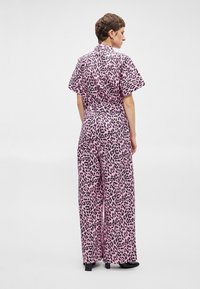 Rózsaszín leopárd mintás overál, rövid ujjú, széles lábú és övvel ellátott derékkal. Sima anyag, fényes felülettel és laza fazonnal.