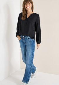 Un haut noir à manches longues avec un décolleté en V et une patte de boutonnage associé à un jean droit bleu. Des baskets argentées complètent le look décontracté.