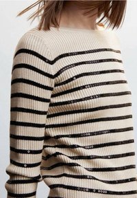 Maglione beige a coste con strisce orizzontali nere. Presenta dettagli in paillettes lungo le strisce. Design a barca, maniche lunghe e forma aderente.