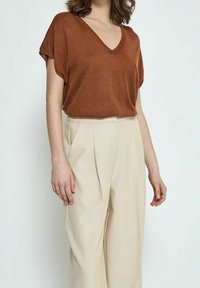 Top de punto metálico bronce con escote en V, combinado con pantalones de tiro alto plisados en beige. El top tiene mangas cortas y un corte relajado.