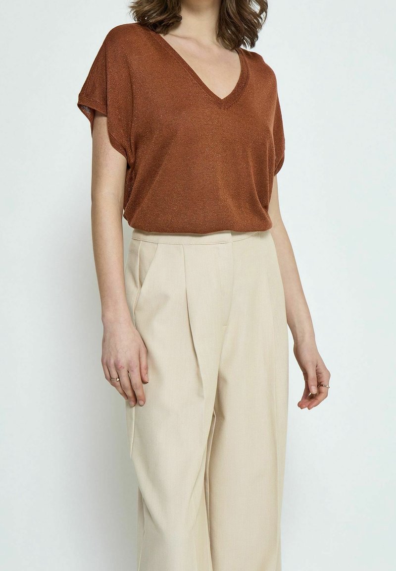 Top de punto metálico bronce con escote en V, combinado con pantalones de tiro alto plisados en beige. El top tiene mangas cortas y un corte relajado.