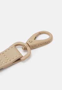 Beige leather strap with metal clasp. Clasp features a circular shape and engraved "VALENTINO." Smooth texture with visible stitching.