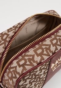 Brun och beige mönstrad handväska med gulddragkedja, logotypdetaljer och släta läderaccenter. Insidan har en enhetlig ljus foder.