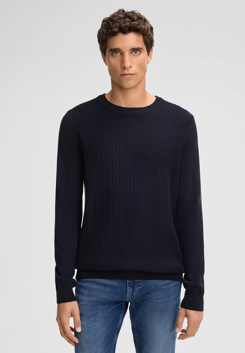 Sweatshirt en maille bleu marine avec un devant texturé, encolure ronde côtelée et manches longues. Associé à un jean en denim ajusté.