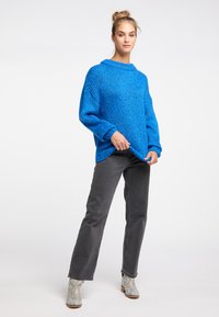 Chunky blue knit sweater with a round neckline and oversized fit, paired with gray straight-leg jeans and patterned ankle boots.