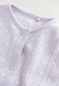 Lila stickad kofta med ett texturerat mönster med små blomsterdetaljer, knäppning framtill och en vågig halsringning. Mjukt tyg.