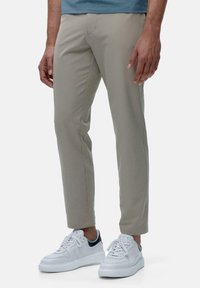 Pantalons slim beige en tissu doux, présentant une texture lisse et des lignes épurées, associés à des baskets blanches avec des accents navy.