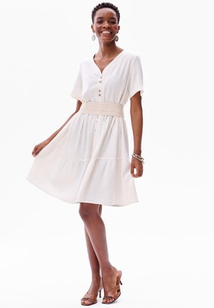 Robe blanche à boutons, avec un col en V, des manches courtes et une taille élastique froncée. Tissu lisse avec une jupe fluide à volants.