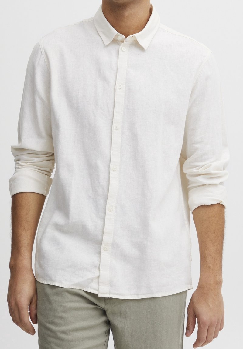 Camicia di lino color crema con colletto button-down, maniche lunghe arrotolate e orlo dritto. Presenta una trama sottile e sei bottoni.
