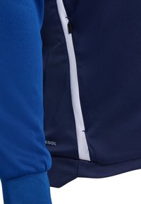 Námornícky modré športové tričko s textúrovanou tkaninou, so zipsovým vreckom a bielymi akcentmi. Obsahuje rebrovaný manžetový lem a branding "COOL" na leme.