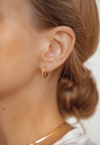 Boucle d'oreille en or avec un petit accent en pierre transparente. Le design est élégant avec une finition polie, mettant en valeur l'oreille.