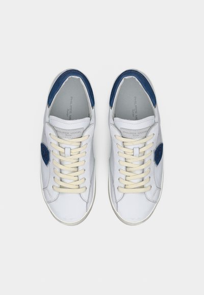 Λευκά αθλητικά παπούτσια χαμηλού παπουτσιού με κρέμ κορδόνια και μπλε λεπτομέρειες στη φτέρνα, φωτογραφημένα από πάνω σε απλό λευκό φόντο.