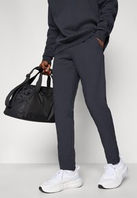 Marineblaue Jogginghosen mit schmalem Schnitt, Taschen und elastischem Bund, kombiniert mit weißen Sneakers und einer schwarzen Sporttasche.