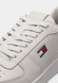 Λευκό δερμάτινο αθλητικό παπούτσι με λευκά κορδόνια, που διαθέτει ένα λογότυπο Tommy Jeans σε κόκκινο, λευκό και μπλε στην πλευρική επιφάνεια.