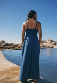 Maxime dress in syvän sininen, jossa on muotoiltu vartalo-osa ja ohuet säädettävät olkaimet. Kelluva kangas laskeutuu nilkkoihin, sopii lämpimille keleille.